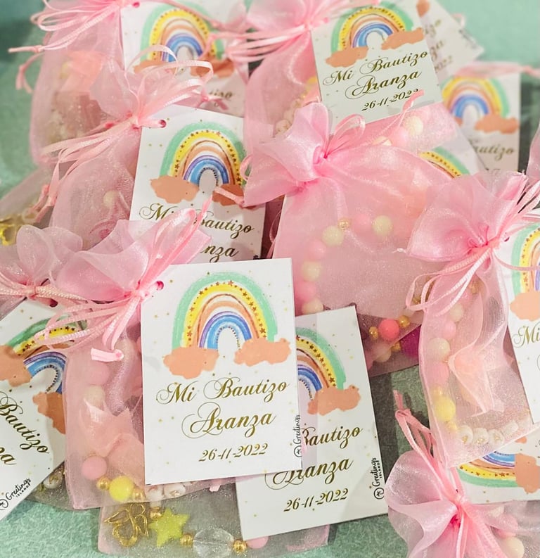Party favors with rainbow tags and pink organza bags containing candy, labeled Mi Bautizo and dated 26-11-2022