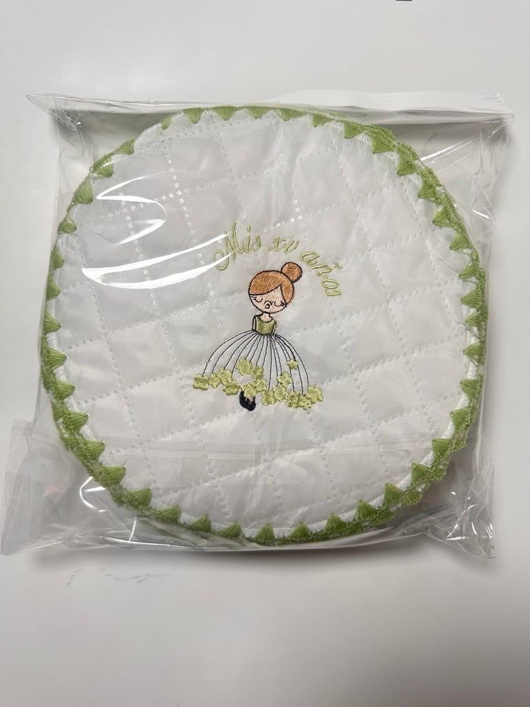 Quilted round pillow in plastic package with embroidered girl in dress and green ruffled trim border