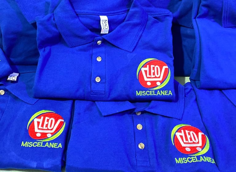 Pila de uniformes de trabajo azules doblados con logo Leo Miscelanea bordado en bolsillos