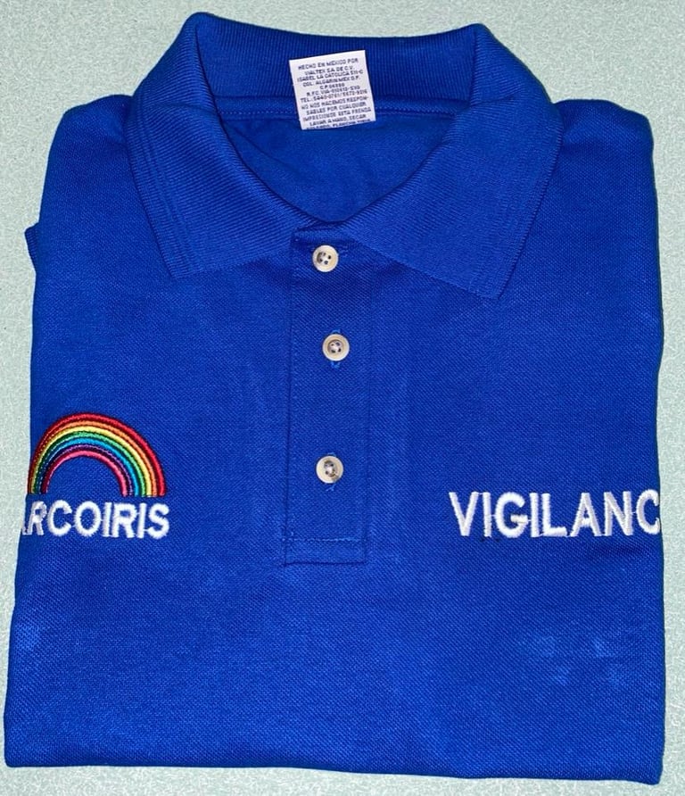 Playera polo azul con logo Arcoiris multicolor en pecho izquierdo y texto Vigilanc a la derecha, doblada