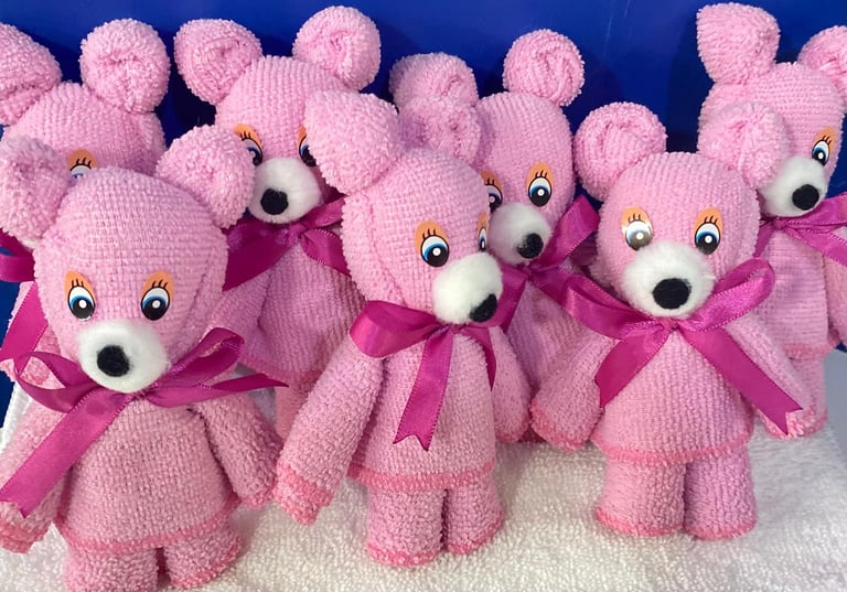Group of pink knitted teddy bears with googly eyes and pink ribbons arranged on blue background