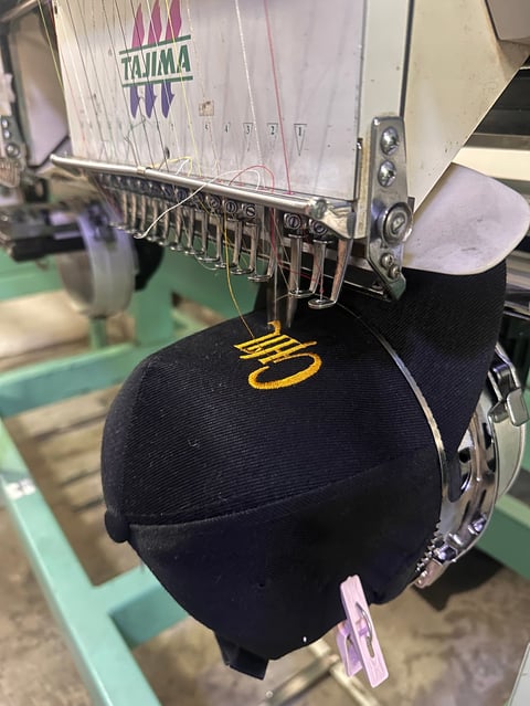 Tajima embroidery machine stitching gold thread on black fabric hat