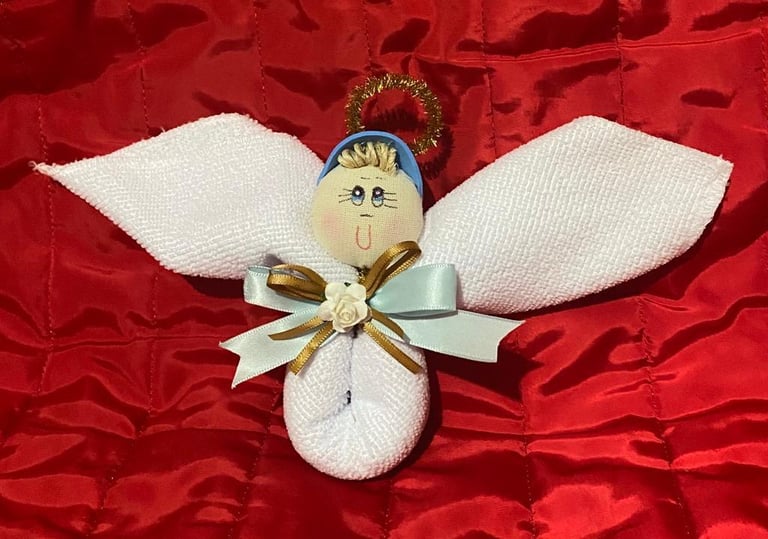 Handmade fabric angel ornament with white wings and gold bow on red velvet background