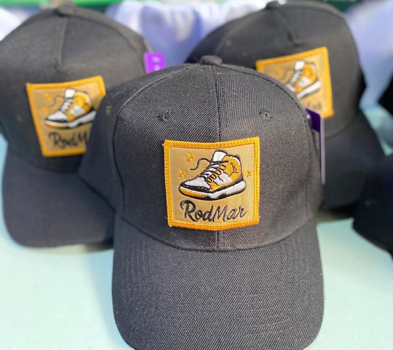 Three black baseball caps with gold patches featuring a sneaker design and RedMax branding