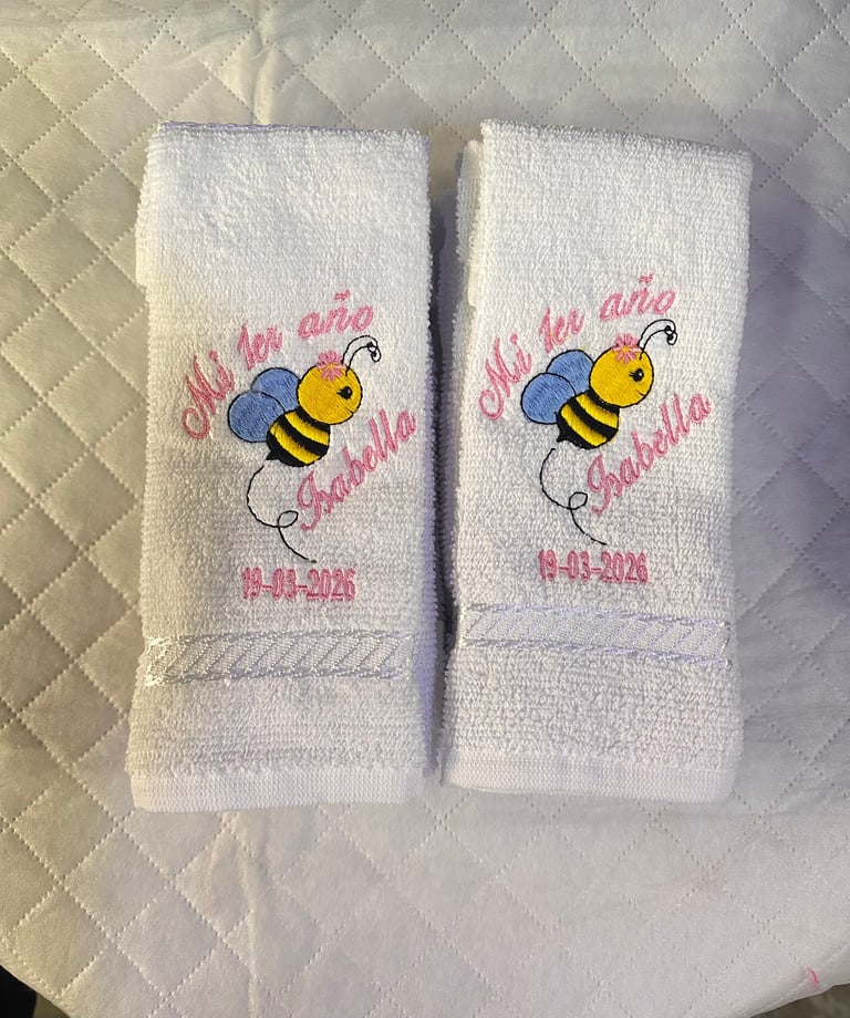 Pair of white embroidered towels with cartoon bees and pink text reading Oh la la abelita and a date