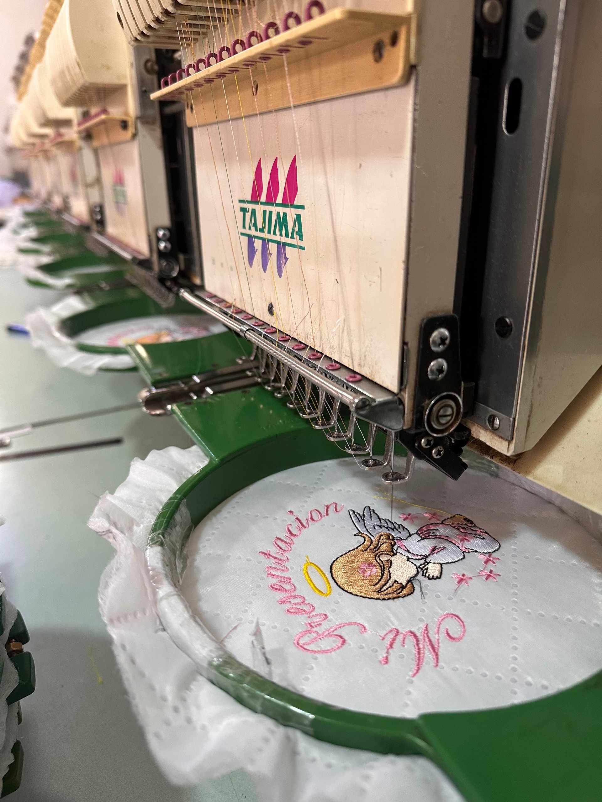 Tajima embroidery machine stitching pink and yellow design on white fabric in green hoop