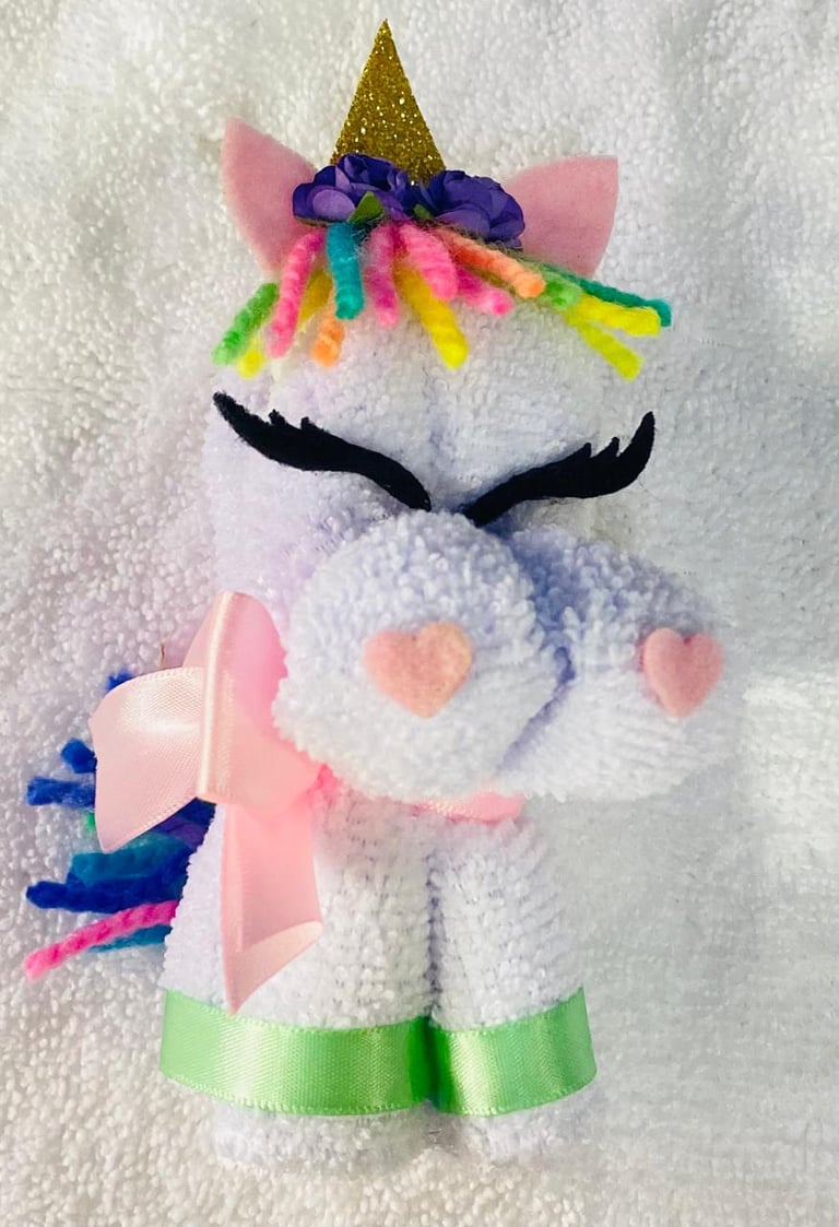 Handmade plush unicorn toy with white fuzzy body, pink ears, gold horn, rainbow mane, black eyelashes, pink heart details, and colorful tail