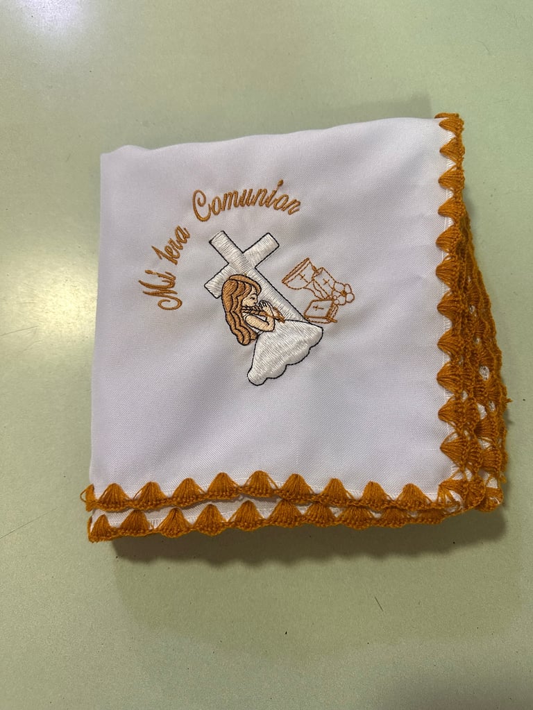 White linen handkerchief with tan embroidered cross, child figure, and Mi Primera Comunion text, trimmed with tan lace border