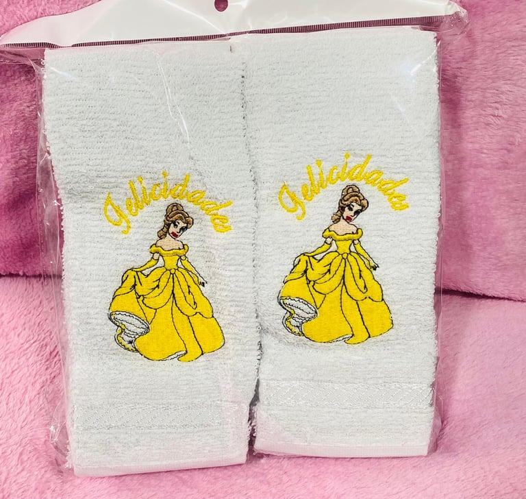Two white towels embroidered with a princess in a yellow ball gown labeled Glittering on a pink background